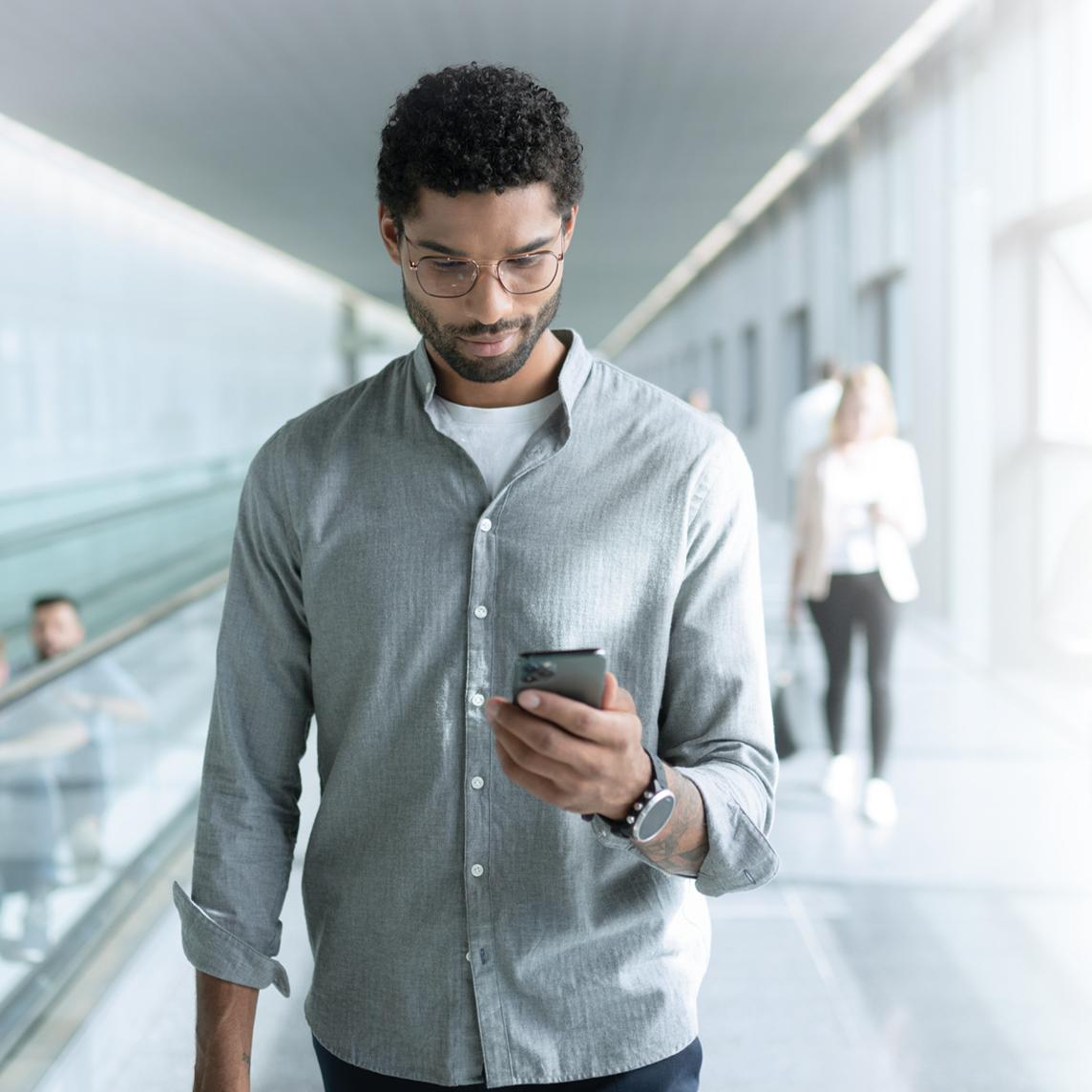 Young man wearing ZEISS SmartLife lenses looking at his phone while walking.