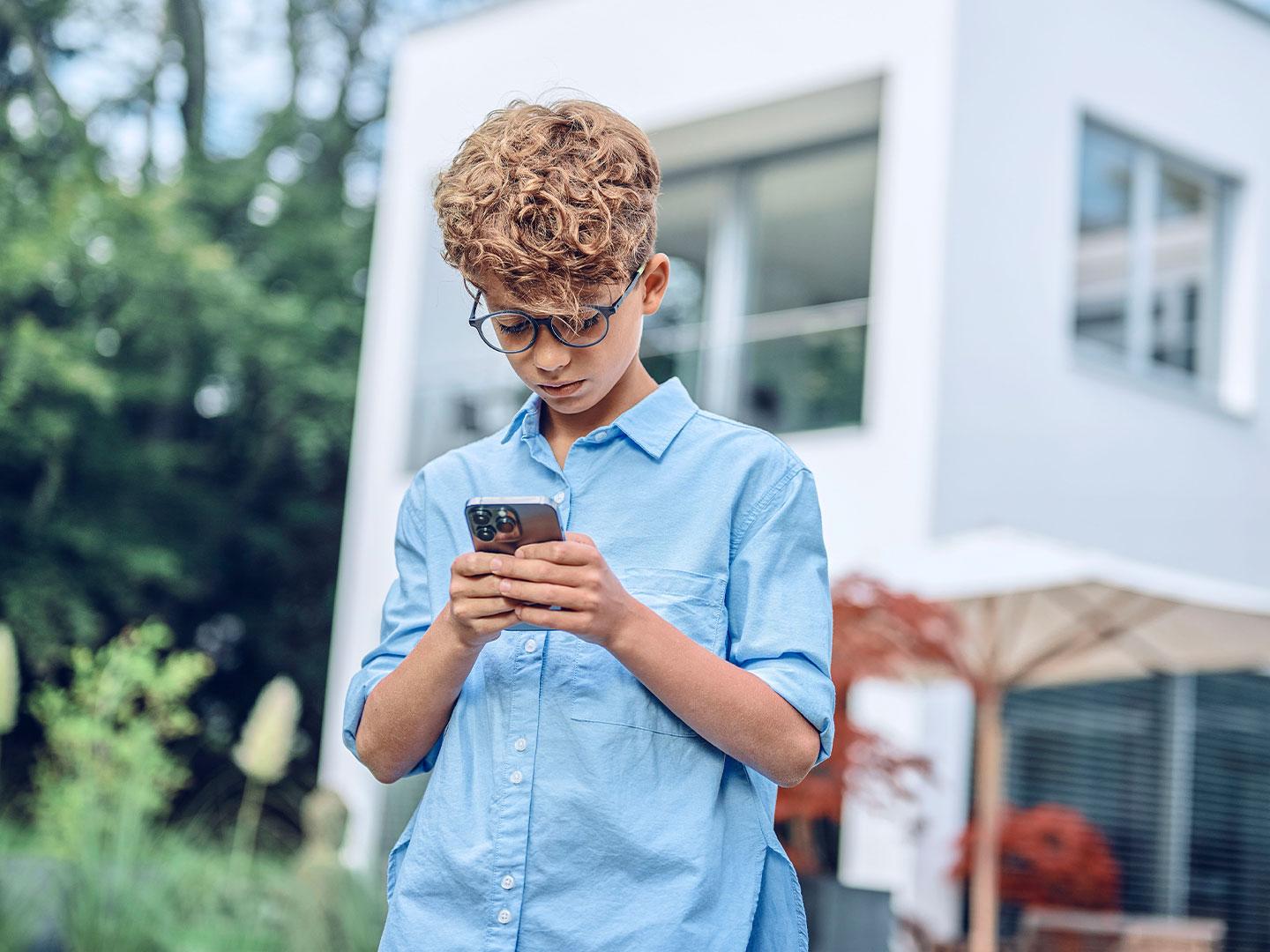 Young boy outside looking at his phone.