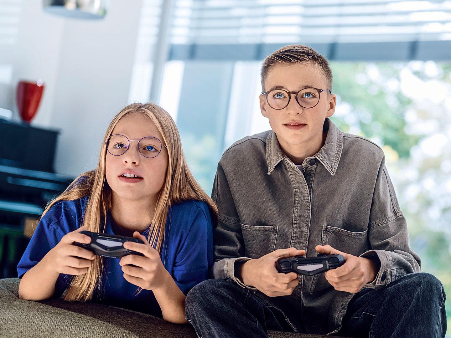 A teenage girl and boy playing video games with consoles.