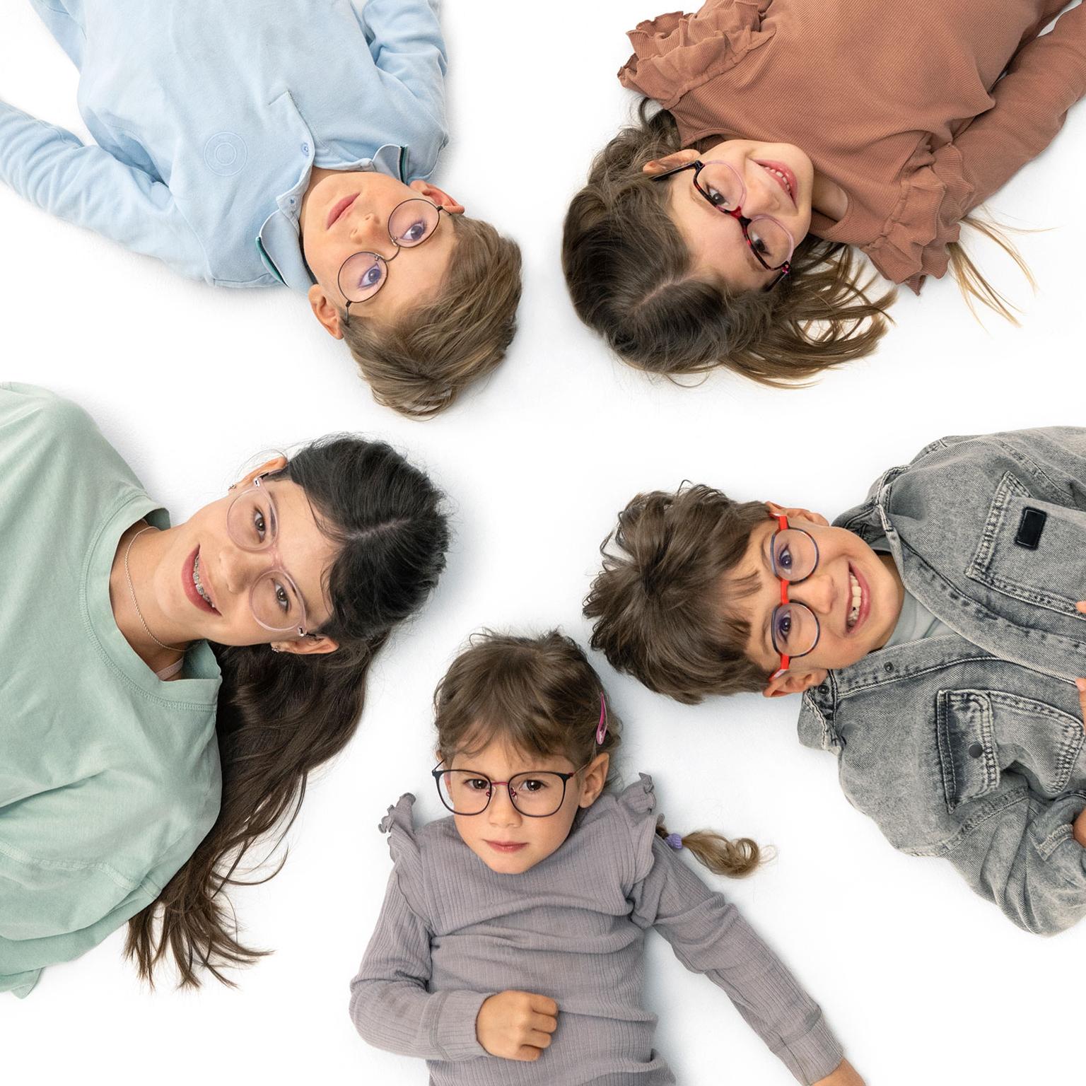 Group of children with glasses laying happily in a circle on the ground