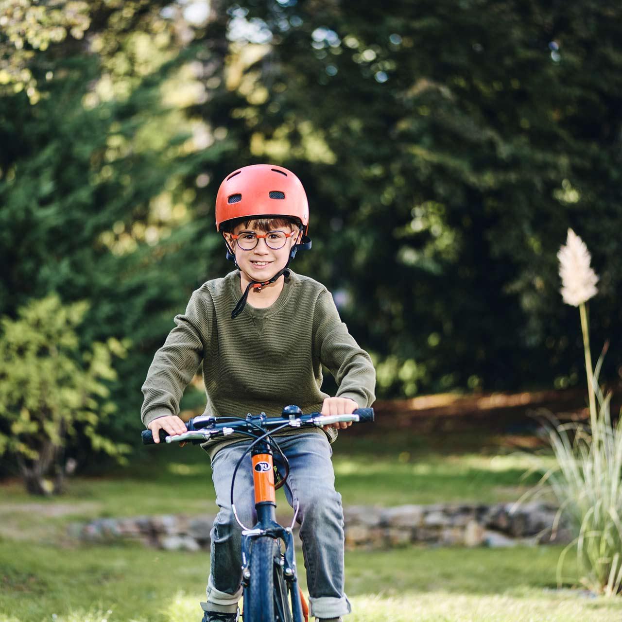 Boy with glasses riding a bike outdoors smiling