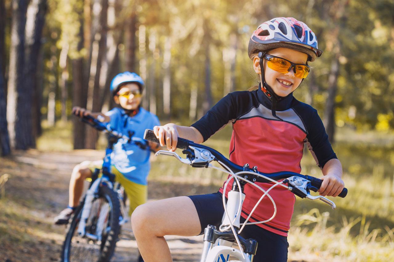 孩子们在阳光明媚的森林里骑自行车 戴头盔在户外骑自行车的儿童