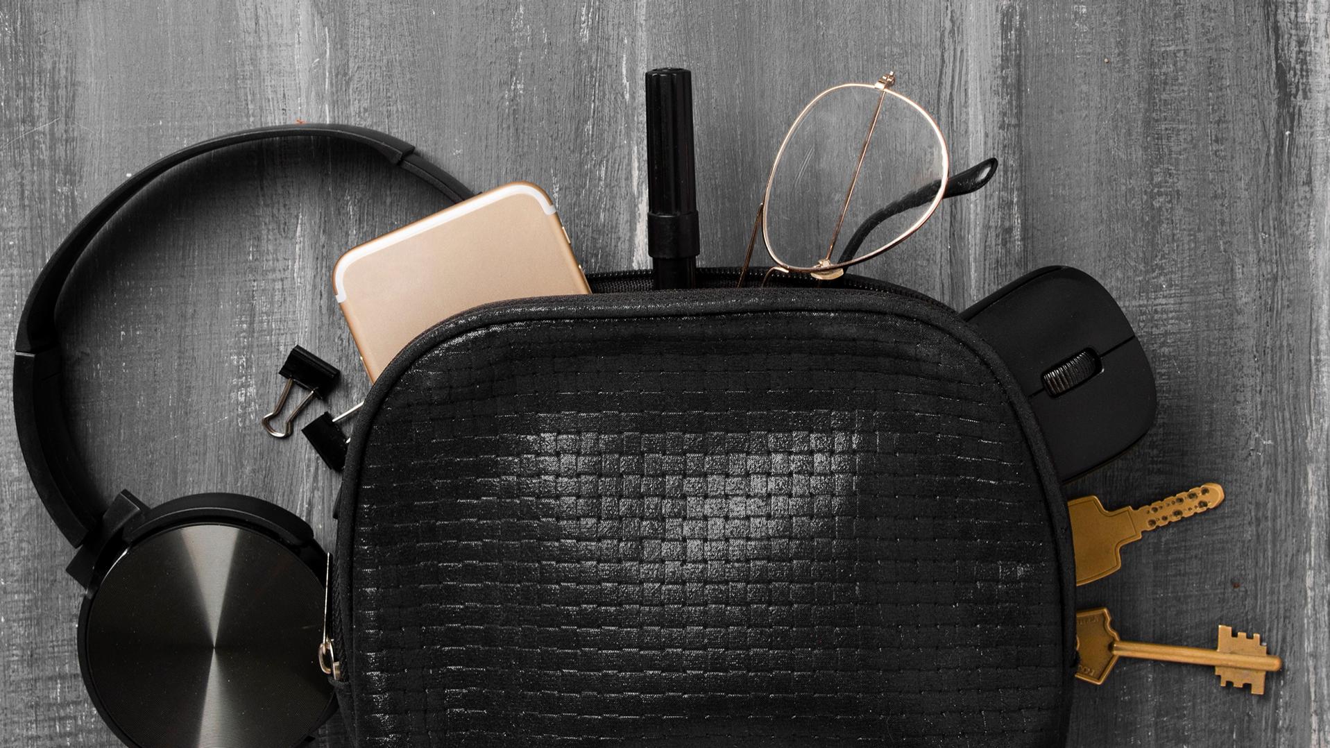 耳機、手機、鑰匙、回形針、筆、電腦滑鼠、配備 DuraVision 鍍膜的蔡司眼鏡從一個黑色小包裡面滑了出來，一半散落在灰色的地板上。