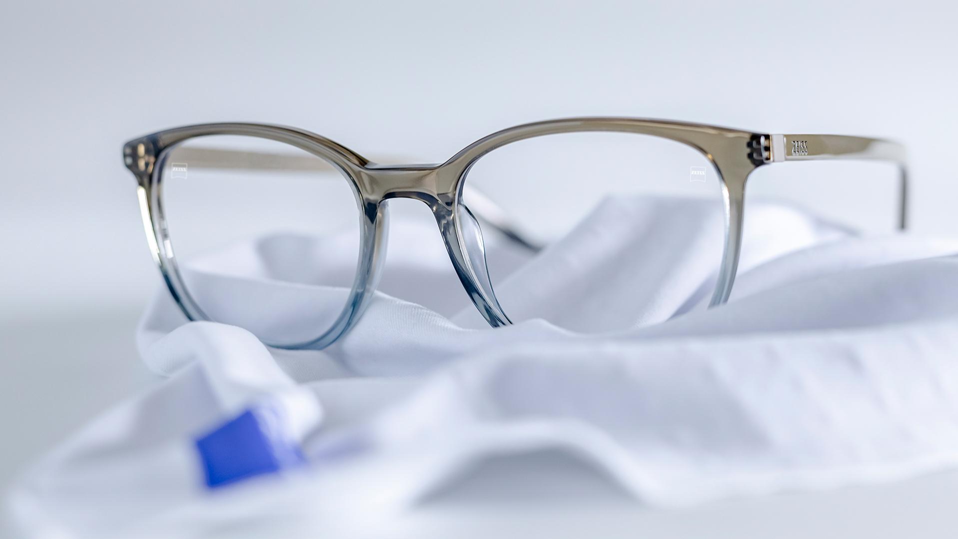 一副配備灰藍色鏡框和 DuraVision® 鍍膜的蔡司眼鏡放在白色超細纖維布上。