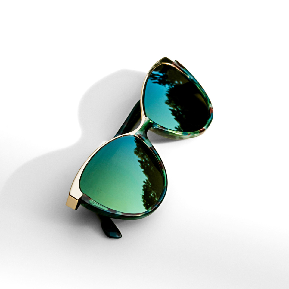 Cat-eye sunglasses with a green mirror effect on a white surface and light shining from the side.