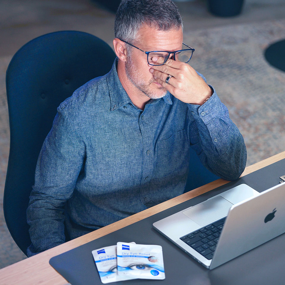 An image of a man in a workspace touching his inner eyes with irritated eyes.
