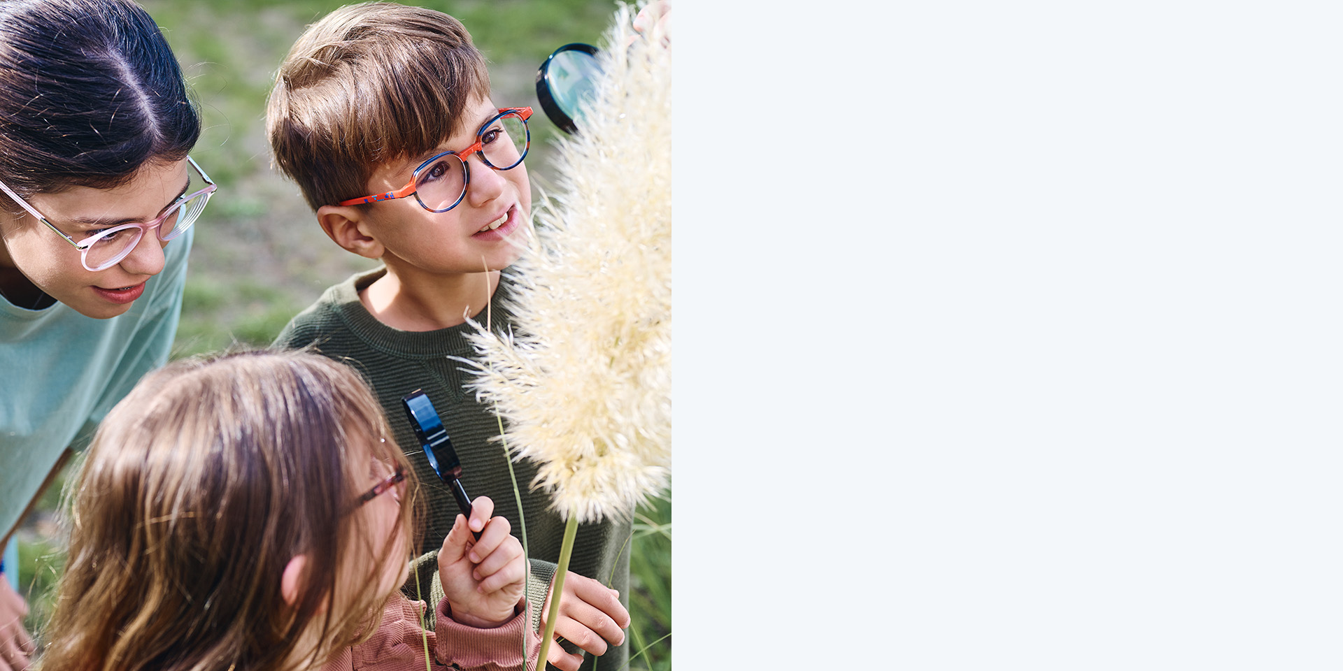 2 個女孩和 1 個男孩配戴蔡司 MyoCare 鏡片。他們看著一棵植物，三個孩童中的兩個 透過放大鏡觀察植物。
