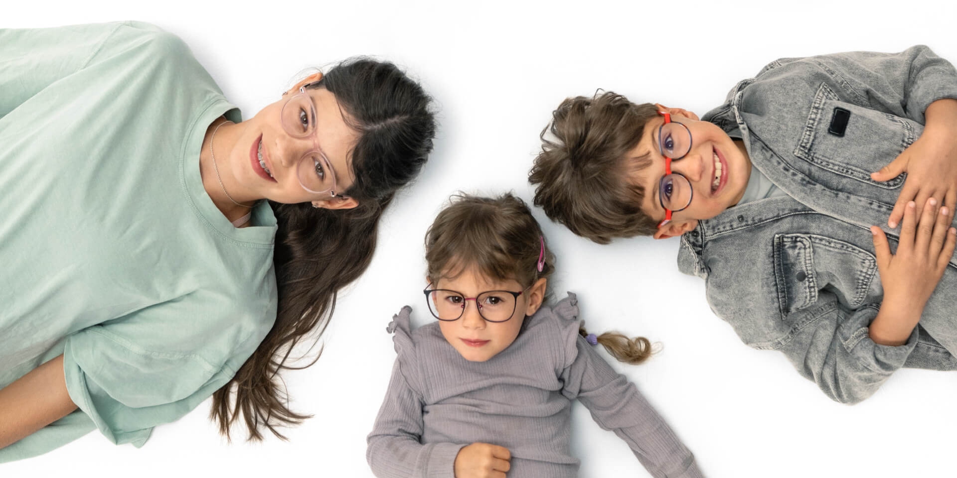 一個青少年和兩個年幼兒童戴著蔡司近視鏡片，躺在地板上。