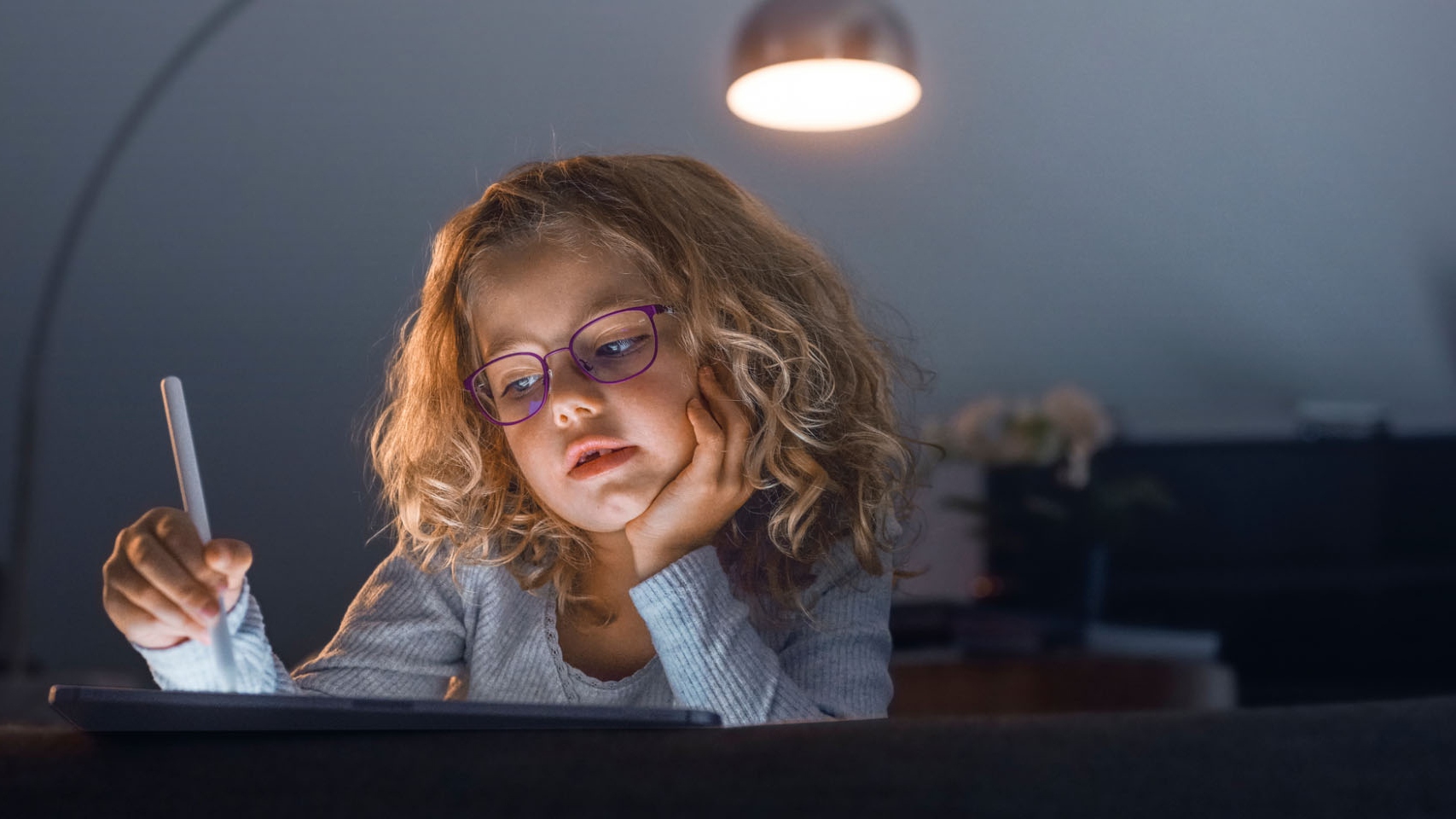 一個小女孩在昏暗的客廳裡看著平板電腦。
